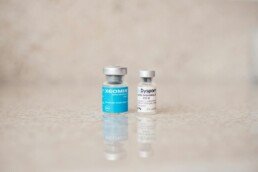 Close-up of Xeomin and Dysport bottles reflecting on a surface, shot indoors.